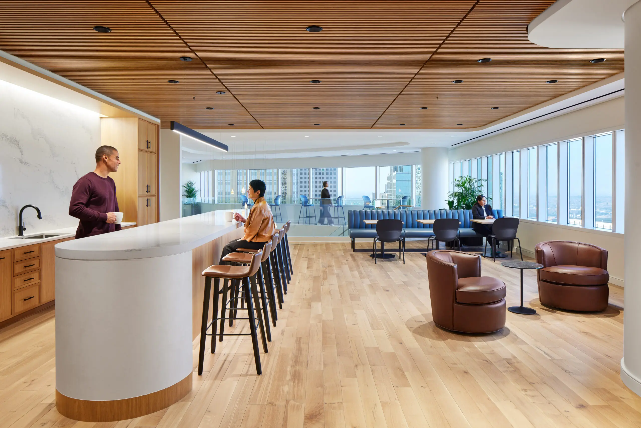 Commercial office lounge with wood slat ceiling, curved bar, and city views