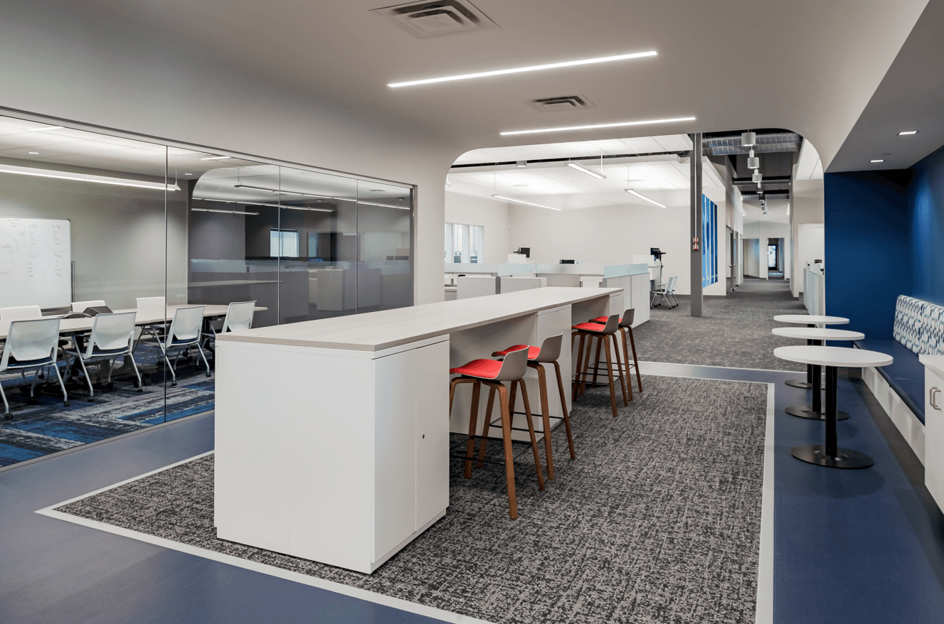 Open commercial office with glass conference room, collaboration counter, and blue booth seating